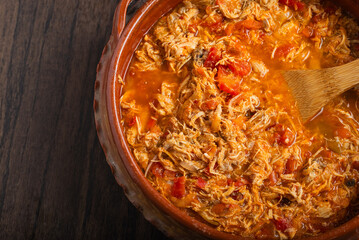 Authentic mexican chicken tinga, typical mexican food prepared in a clay pot on a wooden table.