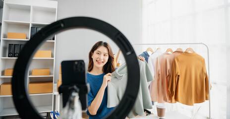 Asian lady blogger showing clothes in front of the camera to recording vlog video live streaming at her shop.&nbsp;Online Shopping