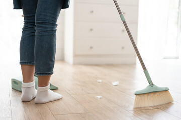 Unknown maid sweep up construction debris with a brush in a dustpan at home	