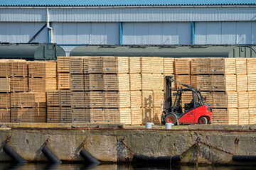Red forklift in the port. Boards on pallets are ready to ship.