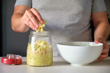 Unrecognizable man putting cabbage into the fermentation jar to prepare homemade sauerkraut.