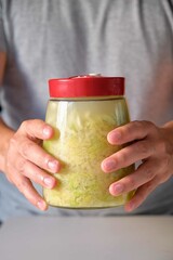 Unrecognizable man holding fermentation jar with homemade sauerkraut or fermented cabbage.
