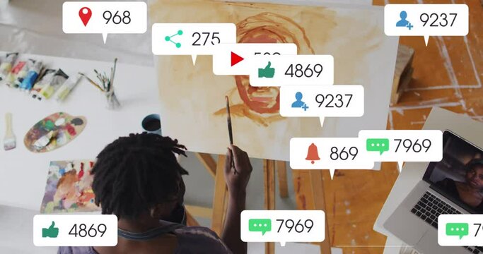 Animation of social media icons on overhead view of african american male artist painting at studio
