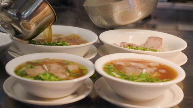 Bowls of pho with broth being poured in a restaurant kitchen, beef pho, Vietnamese food. 4K 24FPS