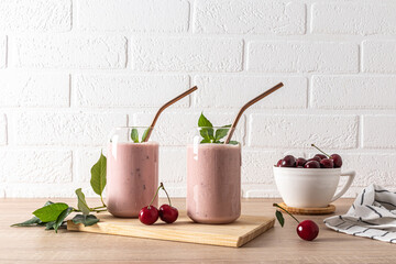 Two stylish glasses with freshly made cherry smoothies and a bowl of ripe cherries on the wooden...