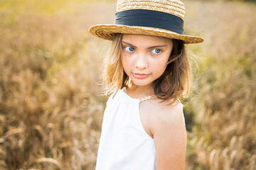 Happy girl walks in beautiful wheat field, embracing summer's yellow sun, nature freedom outdoors. White dress, straw hat, surrounded by rye, barley. Autumn harvest time rural scene.Own piece of land