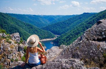 Fototapeta na wymiar Woman traveler with hat looking at beautiful mountain,forest and river view- wanderlust travel concept