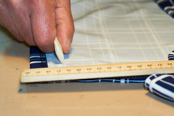 The tailor's hand measures the distance on the fabric with chalk and a ruler