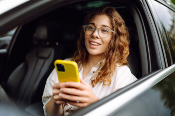 Stylish woman driving a car and using a mobile phone. Navigating the city, lamenting parking. Business, technology concept.