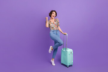 Full length portrait of delighted overjoyed person hold suitcase raise fist achievement luck isolated on purple color background