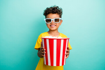 Photo of satisfied schoolboy with brown hair dressed yellow t-shirt hold popcorn at cinema isolated on turquoise color background