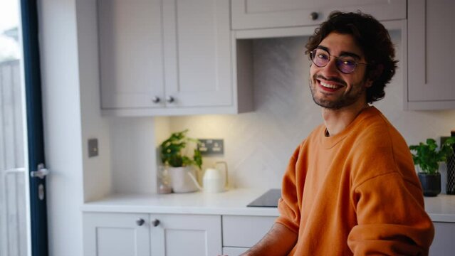 Portrait of smiling young man wearing glasses taking a break sitting at kitchen counter at home - shot in slow motion