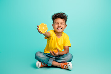 Full size photo of adorable small boy sit floor hold orange slice wear trendy yellow outfit...