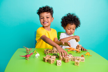 Full size photo of two adorable small boys sit green table nursery toys cubes wear trendy outfit...
