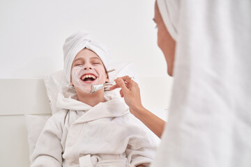 Woman smearing cream mask on face of laughing kid
