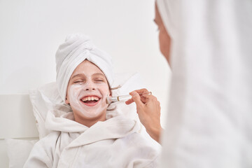Mother applying moisturizing facial mask on laughing child with