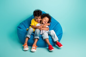 Full body photo of cute little boys sitting soft bean bag embrace hug brothers wear trendy clothes...