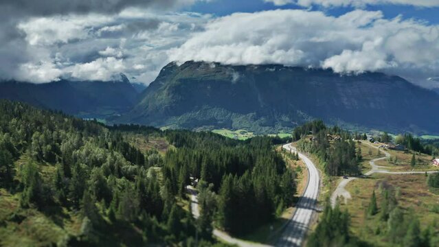 A narrow road winds through the green Norvegian valley of Byrkjelo. Aerial view, pan forward.
