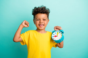 Photo of optimistic schoolboy with brown hair dressed yellow t-shirt hold alarm time to shopping isolated on turquoise color background