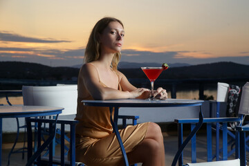 Fashionable young woman holding cocktail with beautiful sunset behind	