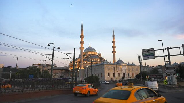 Illuminated New Valide Sultan Mosque at sunset. Cars and taxi driving from the Galata bridge on the foreground. Istanbul, Turkey