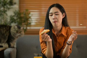 Fototapeta premium Happy young woman sitting on a couch at home, eating pizza. Food, drinks, leisure and holidays concept
