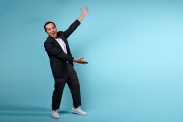 Full length portrait of happy smiling Asian businessman presenting to the side over blue background