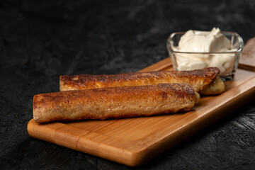 Fried pancakes with sour cream on a wooden board. Dark background
