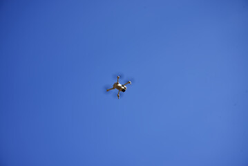 A small quadcopter hovered in the blue sky. Drone in flight.