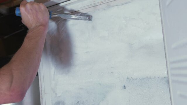 Man chipping away ice from a frozen freezer. Medium Shot