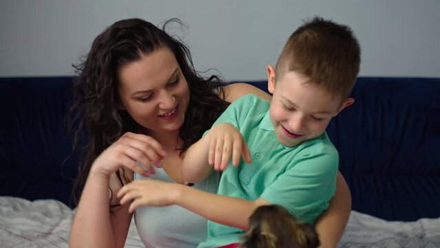 Mom and son are having fun and fooling around in the bedroom on the bed. Happy smiling cheerful family together mom hugs baby. Concept of care and love of parents, happy childhood. High quality 4k 