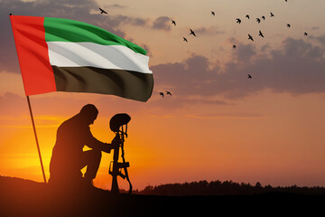 Silhouette of soldier kneeling with his head bowed against the sunrise or sunset and UAE flag....