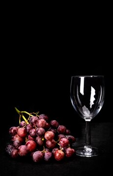 A bunch of red grapes and an empty wine glass on a black background.