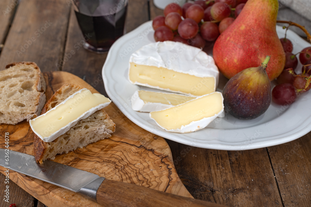 Wall mural Sliced Camembert cheese on piece of bread with fruits and glass of wine in background