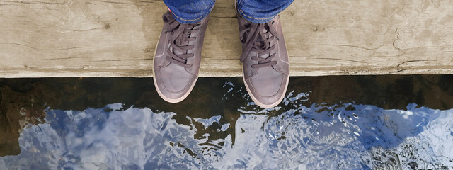 Banner with legs in brown moccasins on background mountain river. Feet of woman or man in brown shoes standing on wooden log above water. Concept of life balance, lifestyle. Header for website, blog - obrazy, fototapety, plakaty