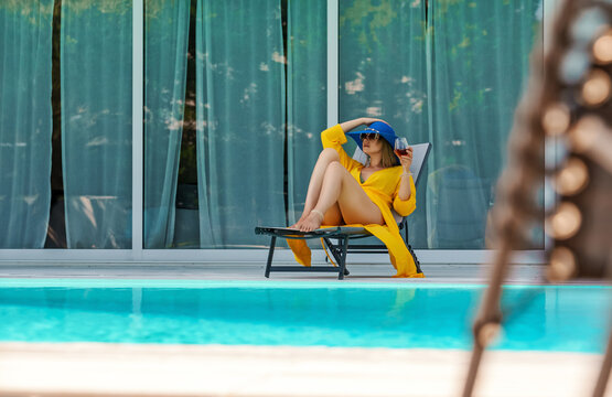 Woman with white glass of wine relaxing near swimming pool.