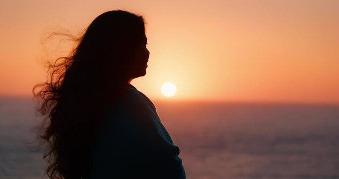 Silhouette of a beautiful Indian woman enjoying the sunset at the sea, with her long hair blowing in the wind
