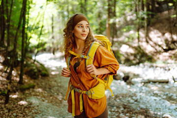 A traveler woman  with a yellow hiking backpack walking along a hiking trail through a forest...