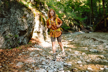 A traveler woman  with a yellow hiking backpack walking along a hiking trail through a forest thicket in the mountains. The concept of travel, hiking. Active lifestyle.