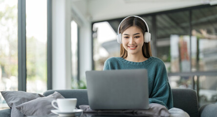 Fototapeta premium Asian teenage girls are happily listening to music from headphone, Asian girls relax by listening to music in the home