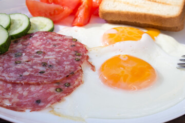 A close-up photograph of a breakfast, featuring fried eggs, salami, croutons.