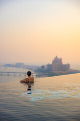 A girl looking over futuristic skyline from rooftop infinity pool during sunset