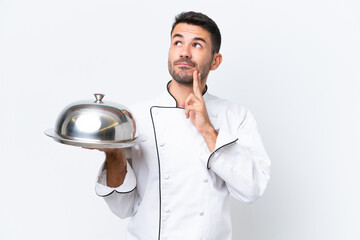 Young chef with tray isolated on white background having doubts and thinking