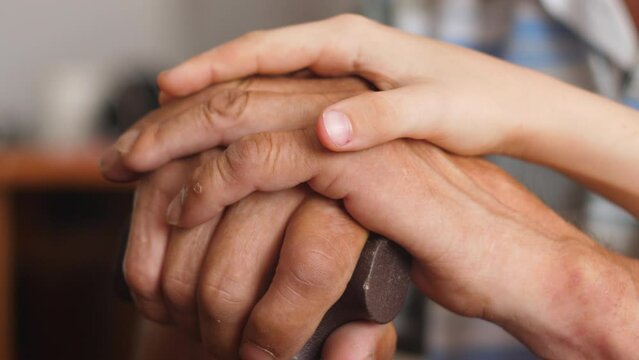  hands of a child stroking the hands of an old man holding a walking stick. support and care for the old man in the family. emotions of old people and children. friendship between grandparents 