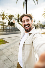 Vertical portrait of cheerful happy young man smiling looking at camera taking a selfie in the...