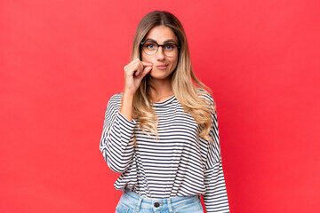 Young Uruguayan woman isolated on red background showing a sign of silence gesture