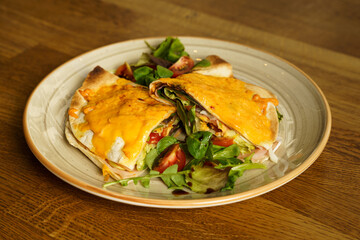 Ham and cheese tortilla sandwich with vegetables on a wooden table