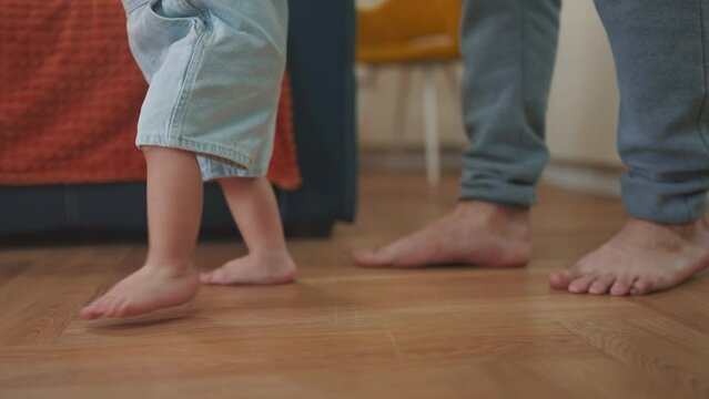 baby first steps. daddy a teaches baby toddler son to take first steps. happy family kid dream concept. baby indoors learning to walk father holding child hands. lifestyle fathers day concept