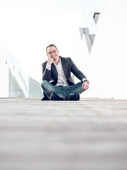 Cheerful businessman sitting on street and leaning on hand