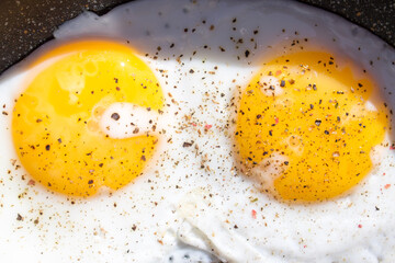 Freshly fried eggs with peppers in a frying pan close-up.